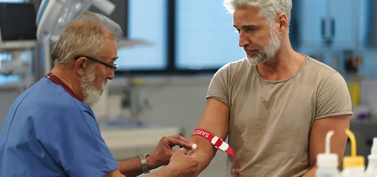 Older man sitting in clinic having a blood test as a clinician prepares the sample for diagnostics.