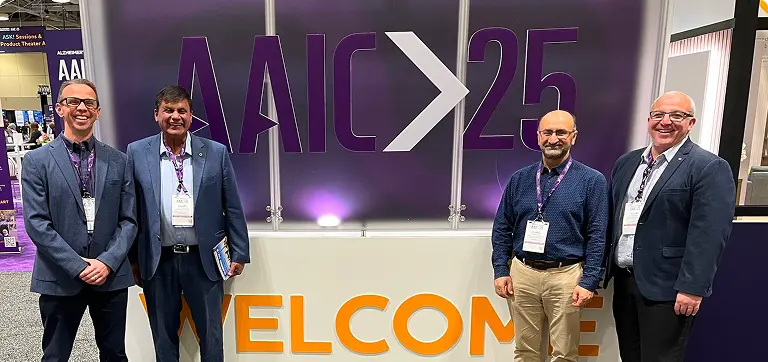 Four men at AAIC25 by a welcome sign for Smart Minds Dx, discussing dementia diagnostics and an Alzheimer's blood test.